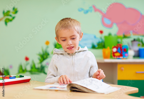 cute boy, kid with special needs looking at a book, in rehabilitation center