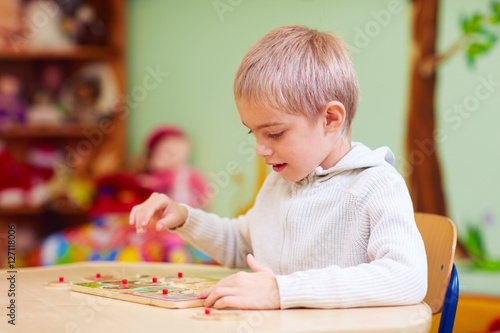 Photos cute boy, kid with special needs solving a puzzle in rehabilitation center