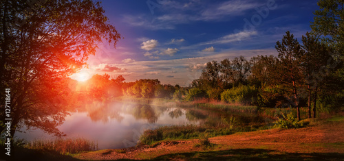 foggy sunrise over Lake in the spring forest. Fantastic  landscape over the river under Shining Sunlight. majestic picturesque sunset. Dramatic scenic summer scene. Beauty in the world © jenyateua