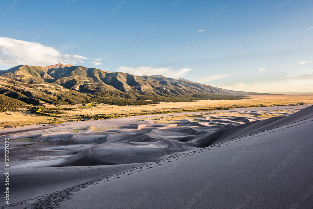 Great Sand Dunes in Colorado with footprints trail path and mountains during sunset