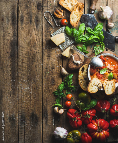 Homemade Italian roasted tomato and garlic soup in bowl with basil and Parmesan cheese over old rustic wood background, top view, copy space, verticall composition photo