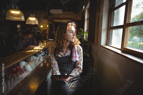Thoughtful waitress looking through window in cafe photo