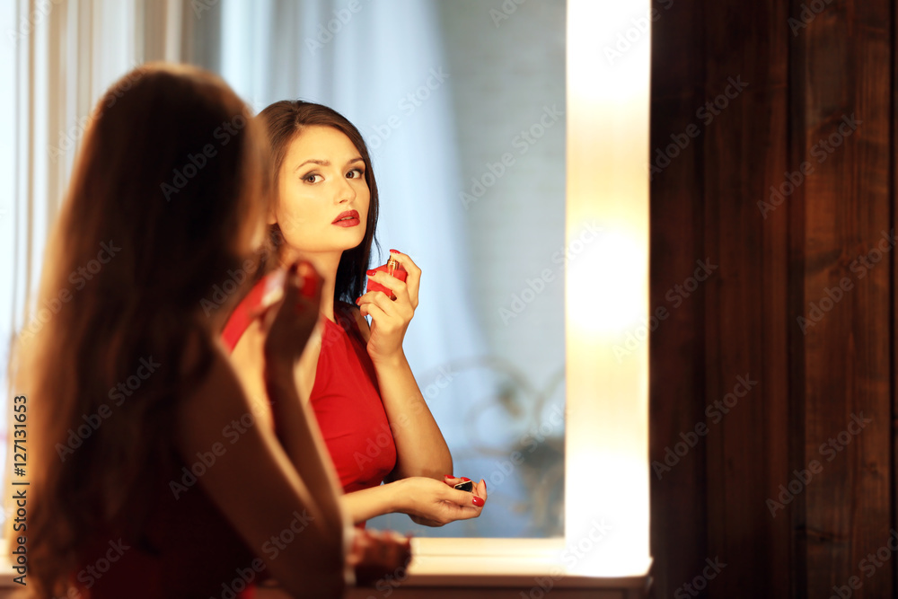 Beautiful girl applying cosmetics in front of mirror