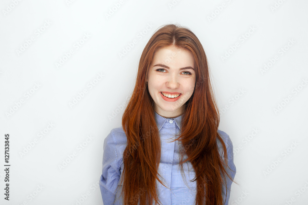 Portrait of cute redhead girl wearing blue striped shirt smiling with happiness and joy while posing against white studio background. Headshot of cheerful female with happy expression