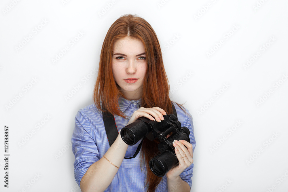 Portrait of cute redhead girl wearing blue striped shirt smiling with happiness and joy while posing with binoculars against white studio background Portrait of cute redhead girl wearing blue striped shirt smiling with happiness and joy while posing with binoculars against white studio background