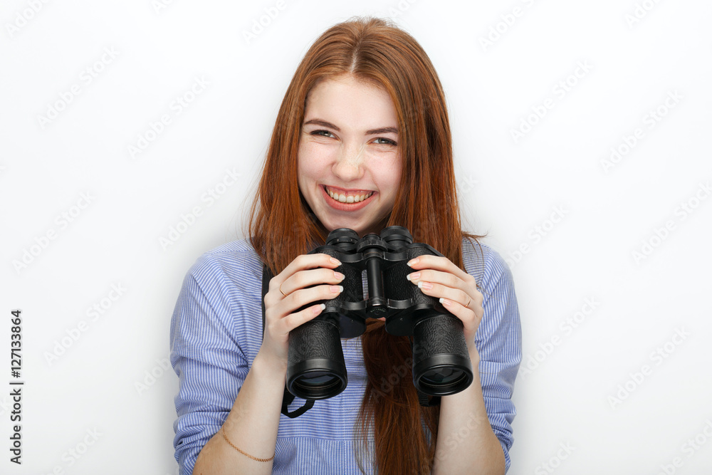 Portrait of cute redhead girl wearing blue striped shirt smiling with happiness and joy while posing with binoculars against white studio background Portrait of cute redhead girl wearing blue striped shirt smiling with happiness and joy while posing with binoculars against white studio background