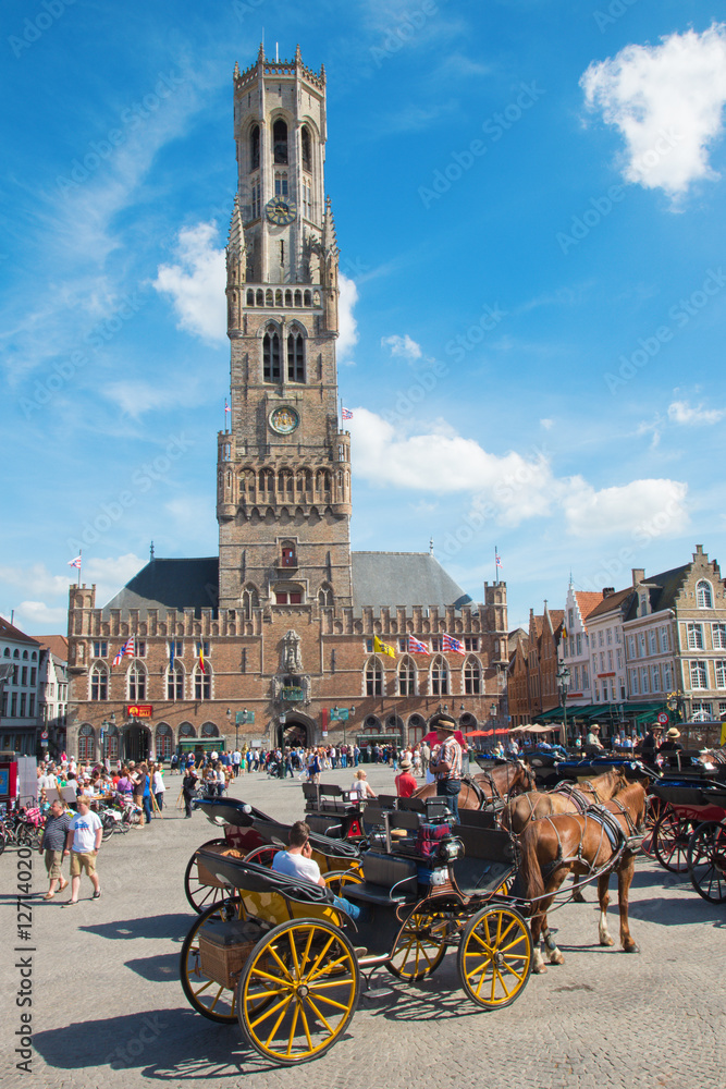 Fototapeta premium BRUGGE, BELGIUM - JUNE 13, 2014: The Carriage on the Grote Markt and Belfort van Brugge in background.
