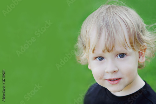 Slika na platnu Portrait of a blond curly-headed boy on green background, close-up, copy space