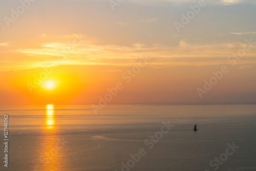 Burning sunset overlooking the ocean and a lonely boat.