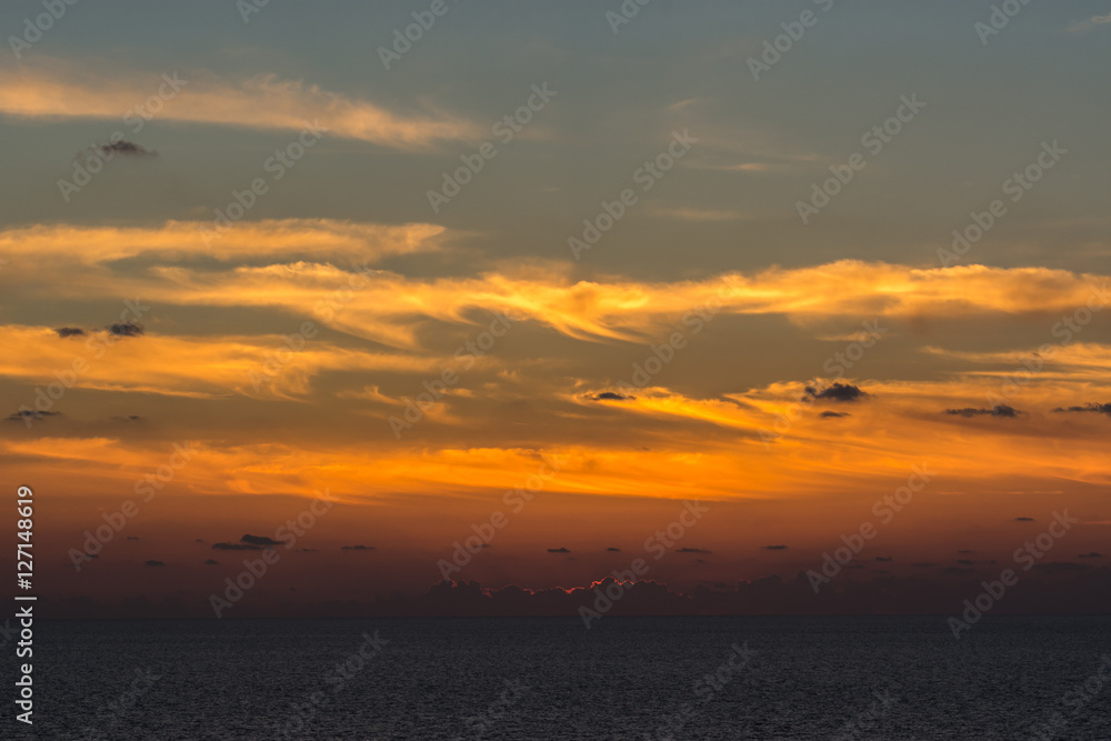 Flame-like orange sunset light over high cirrus clouds at sea