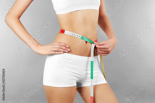 Woman measuring her waist on color background