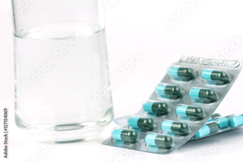 Glass of water and medicine capsule on white background