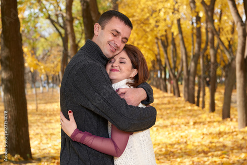 romantic people, happy adult couple embrace in autumn city park, trees with yellow leaves, bright sun and happy emotions, tenderness and feelings © soleg