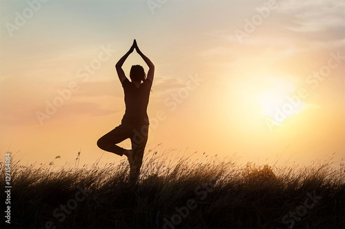 silhouette of woman practicing yoga on the nature at sunset background