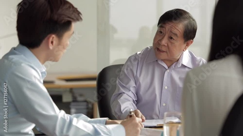MS SELECTIVE FOCUS Senior businessman in discussion with two colleagues at meeting table / Singapore