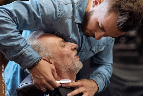 Attractive hairdresser is shaving male beard with the knife