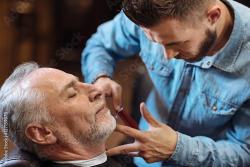 Handsome young barber cutting mustache of senior client with scissors