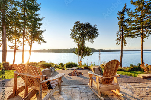 Back yard of waterfront house with adirondack chairs and fire pit photo