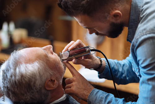 Side view of young barber trimming beard