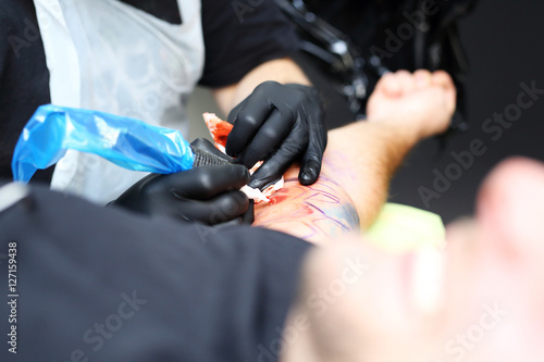 Tatuażysta tatuuje kolorowy tatuaż na ręku mężczyzny