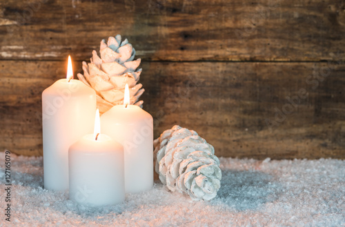 Weihnachtsdekoration weiße Kerzen und Zapfen im Schnee