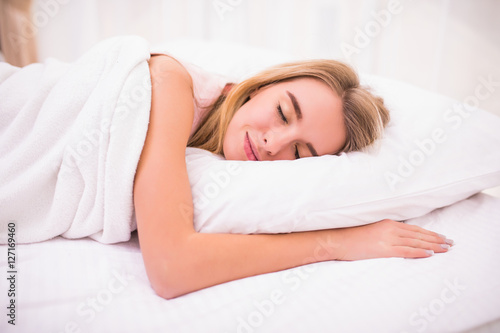 view of tired beautiful young woman with long hair sleeping on bed in bedroom