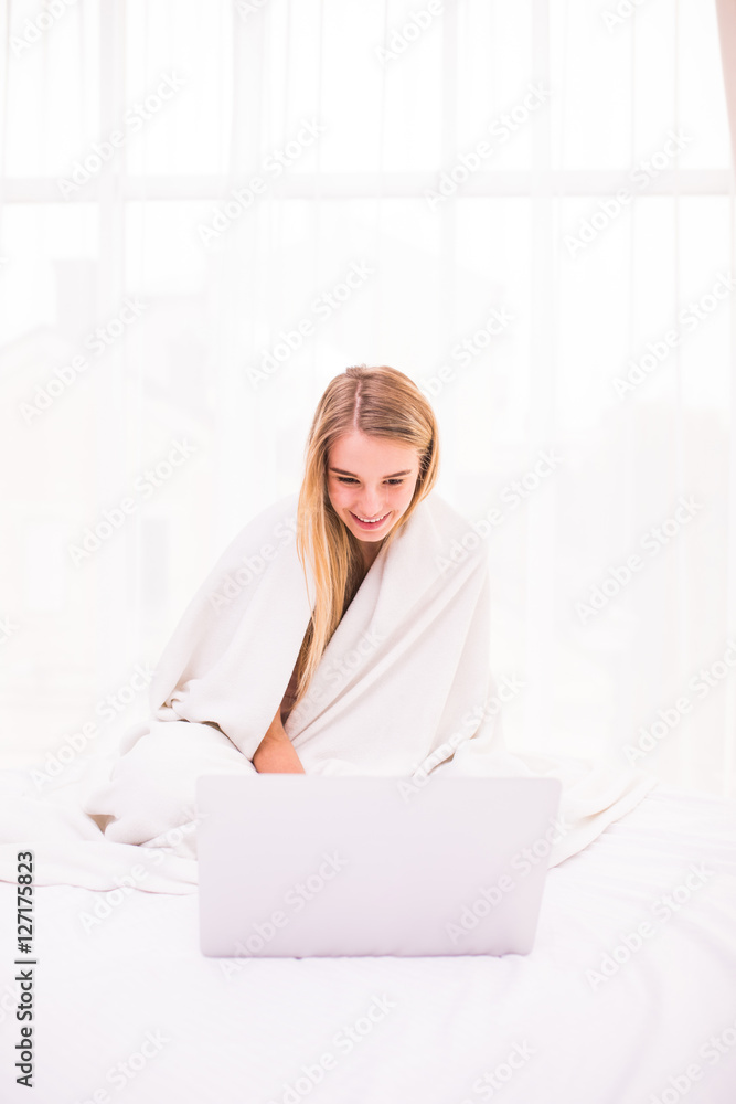 Attractive young woman lying on bed under coverlet and using laptop Attractive young woman lying on bed under coverlet and using laptop