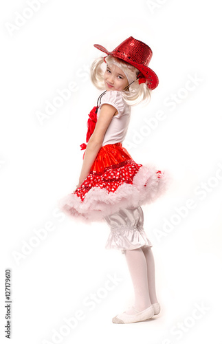 Cute little caucasian girl wearing red skirt, t-shirt with flowers and cowboy hat isolated on white background. She is dancing.