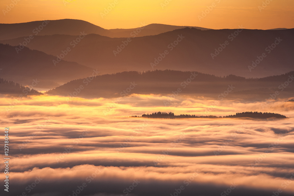 Summer weather phenomenon. Seasonal landscape with morning fog in valley. Clouds drenched valley below the level of the mountains. Sunrise over creeping clouds.