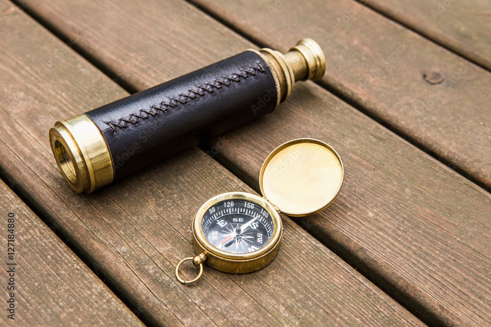 Ancient telescope and compass on wooden background
