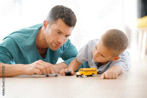 Daddy with son playing with car toys, laying on floor