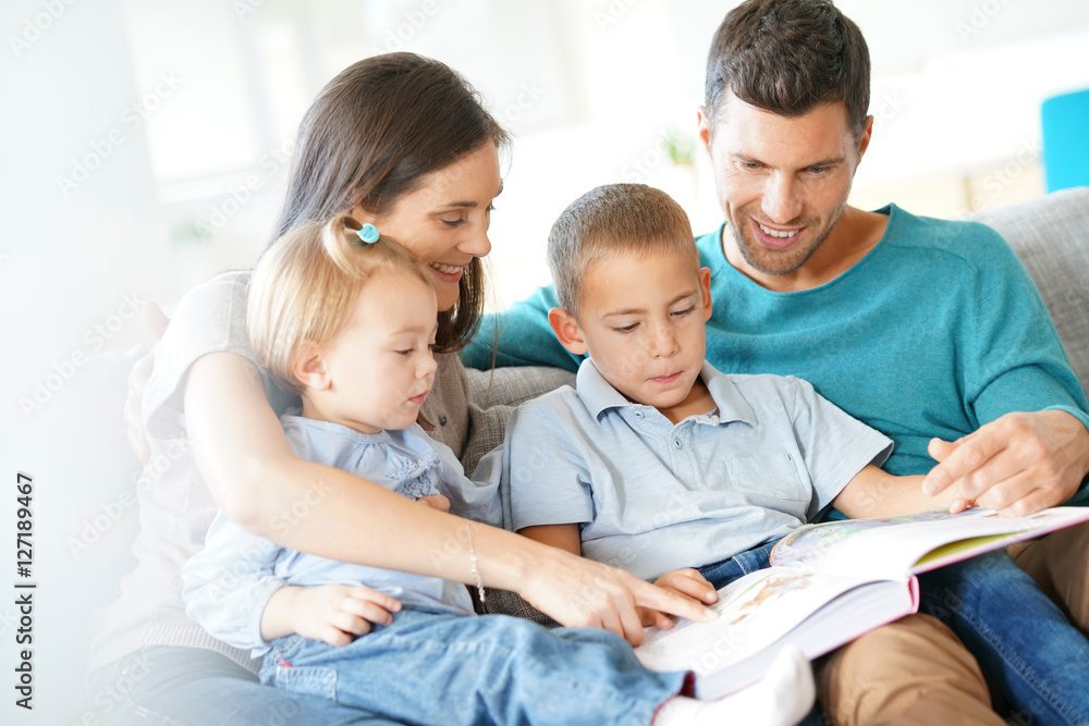 Family sitting on sofa reading book with kids