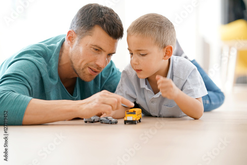 Daddy with son playing with car toys, laying on floor