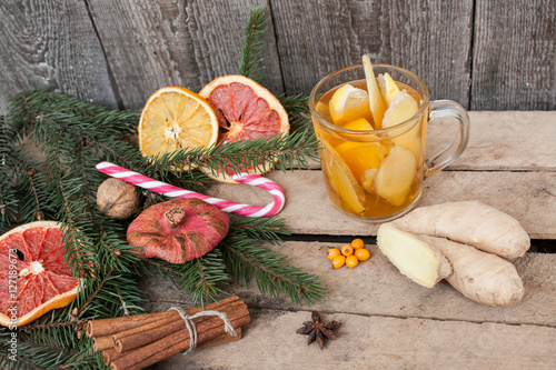 Christmas composition. Spruce branches, candy cane, warming tea with ginger and lemon, dried oranges, grapefruit, cinnamon, Christmas toys, walnuts, star anise, pomegranates on a wooden background.
