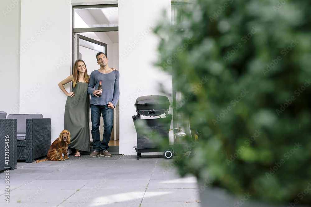 © Westend61 - Smiling couple with dog standing at terrace door © Westend61 - Smiling couple with dog standing at terrace door