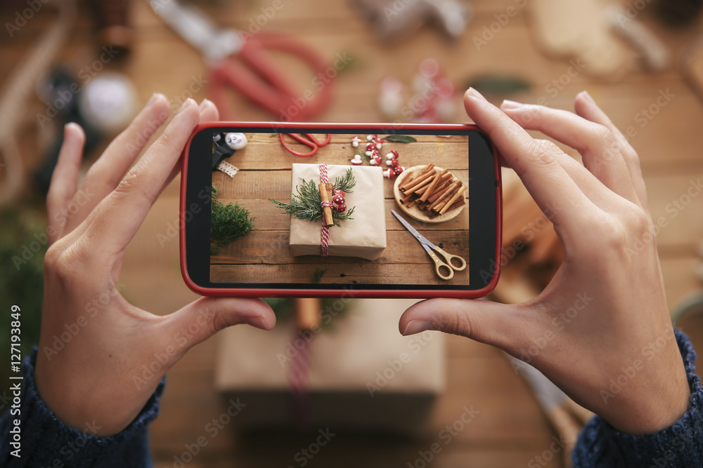 Woman photographing decorated Christmas gift with smartphone, close-up Woman photographing decorated Christmas gift with smartphone, close-up