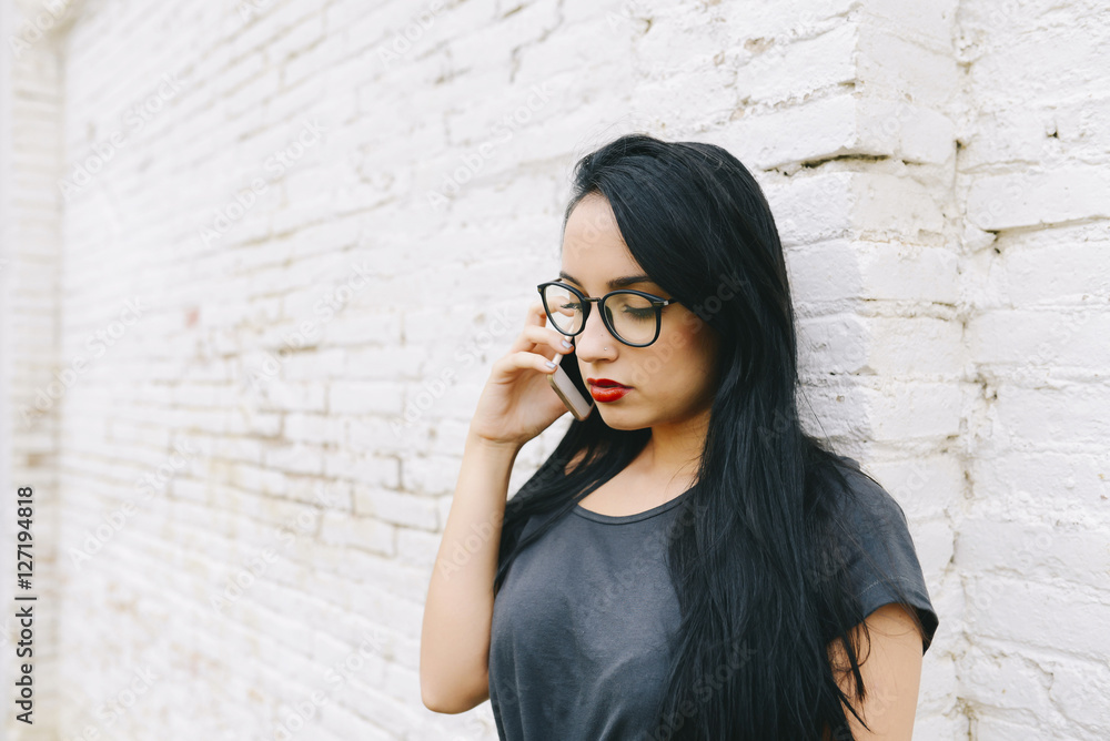 Young woman on cell phone in front of brick wall Young woman on cell phone in front of brick wall