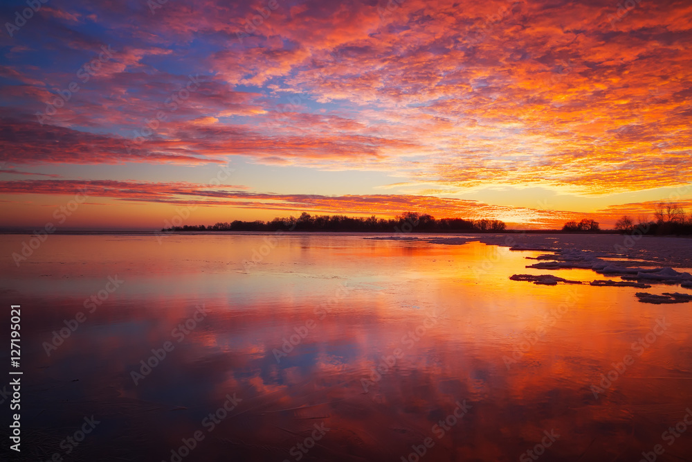 Beautiful winter landscape with sunset fiery sky and frozen lake
