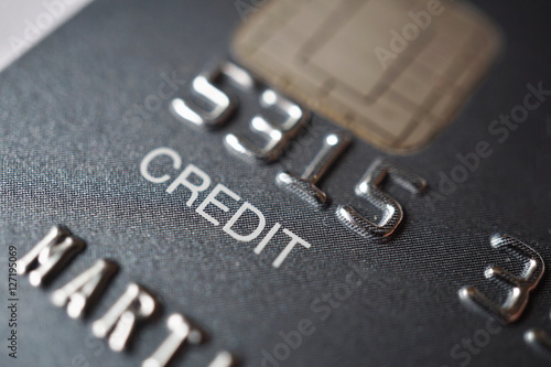 Isolated macro detail of a brand new black and gray luxurious credit card with focus on the caption Credit, metal electronic chip and embossed numbers and letters 