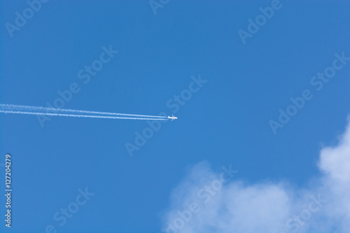 Plane with exhaust stripe across a blue sky with cloud