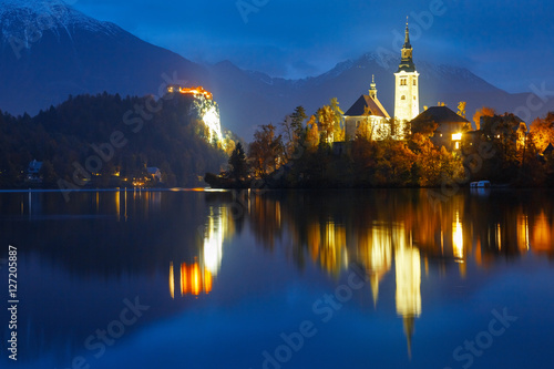 View of famous island, castle rock and town Bled illuminated at the night and reflected in lake surface water. Location: Bled lake, Slovenia. Night scene.