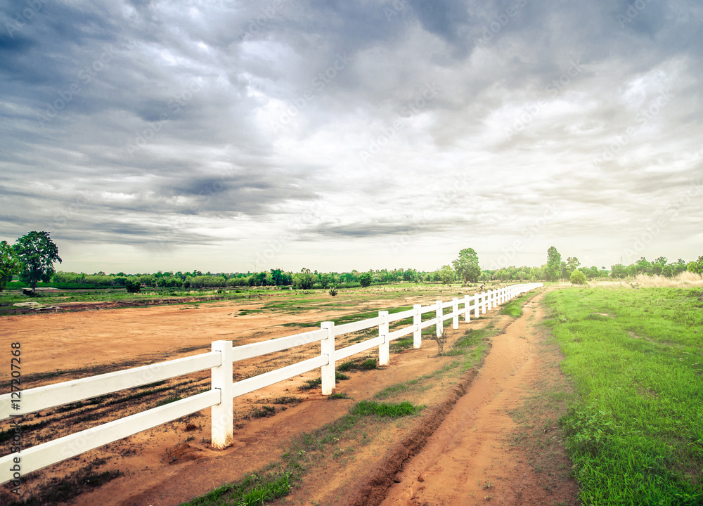 white fence in farm field and overcast sky