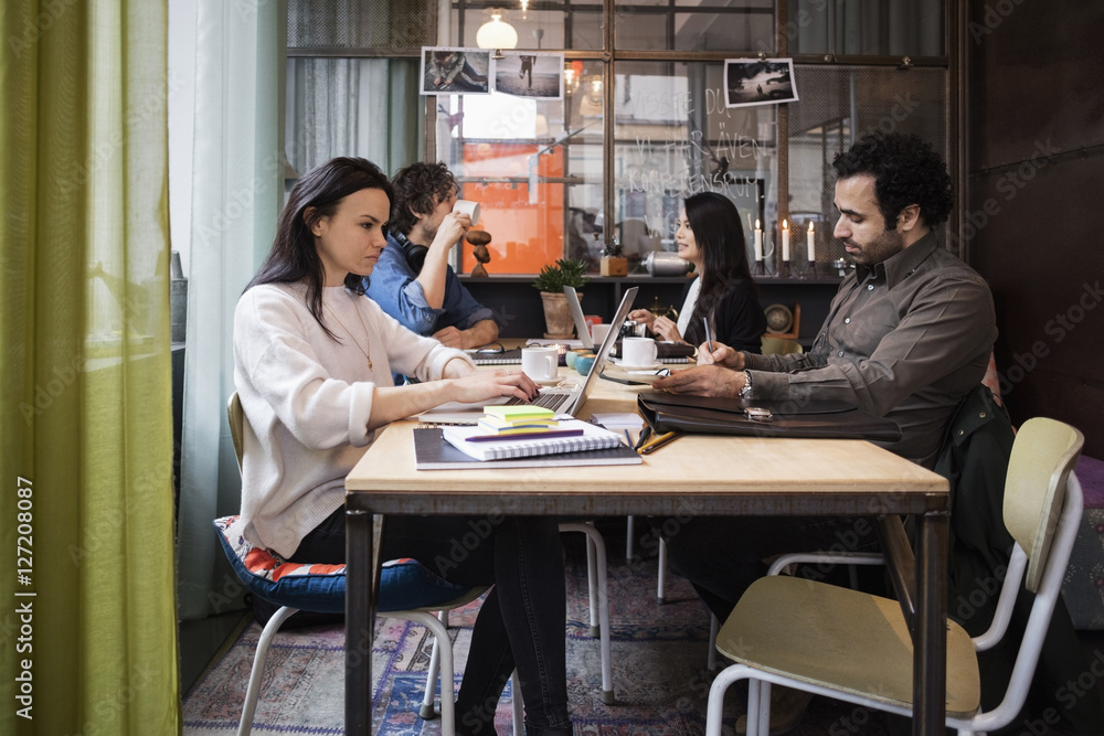 Creative business people working while sitting at table in office Creative business people working while sitting at table in office