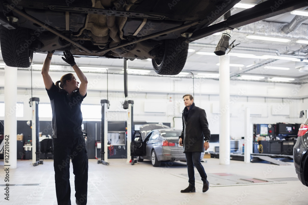 Mechanic looking at customer while working under car at repair shop Mechanic looking at customer while working under car at repair shop