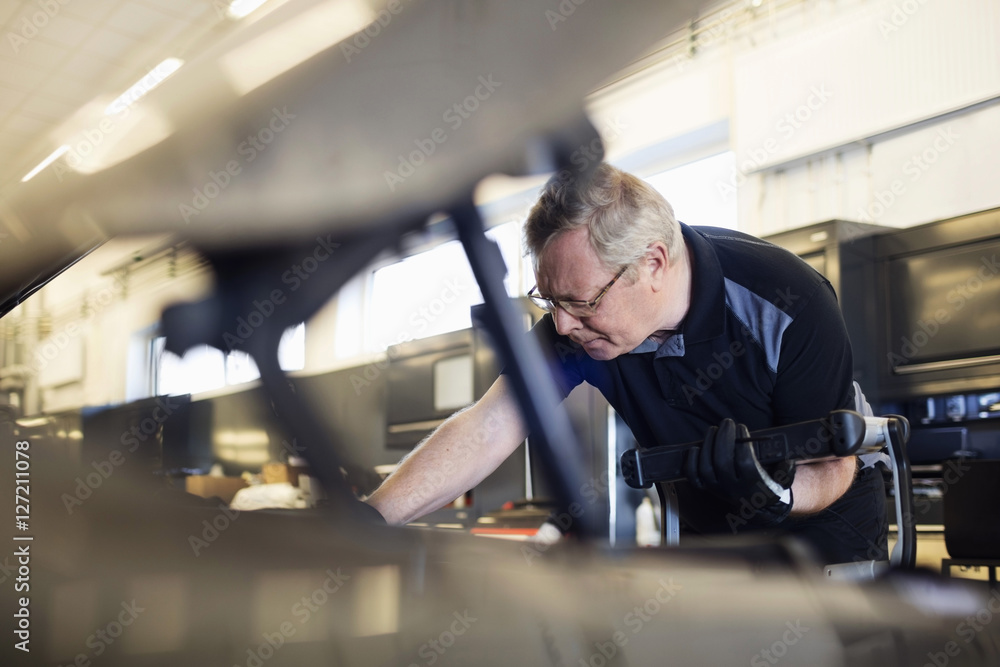 Senior mechanic holding technology while examining car