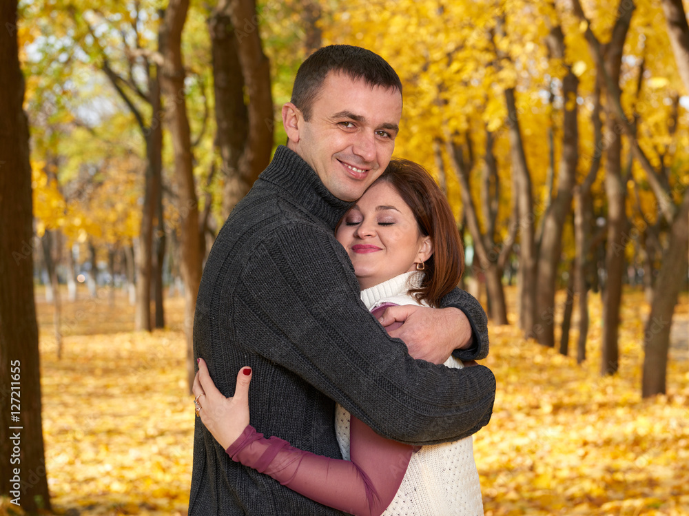 Fototapeta premium romantic people, happy adult couple embrace in autumn city park, trees with yellow leaves, bright sun and happy emotions, tenderness and feelings