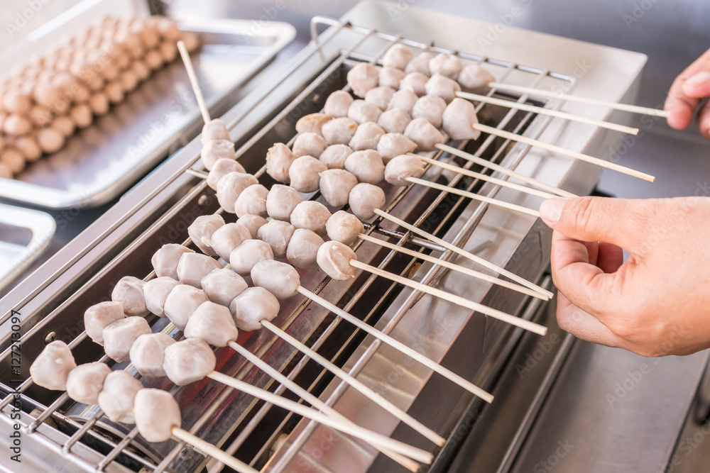 Close up scene : grilled pork meatball skewers on electric roaster 
Thai meat ball with bamboo stick, cooking food sold by vendors in a street or other public location for immediate consumption