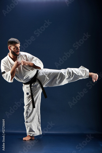 Karate man in a kimono hits foot on a blue background