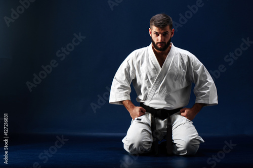 Karate man in a kimono sits on her knees on the floor on blue background photo