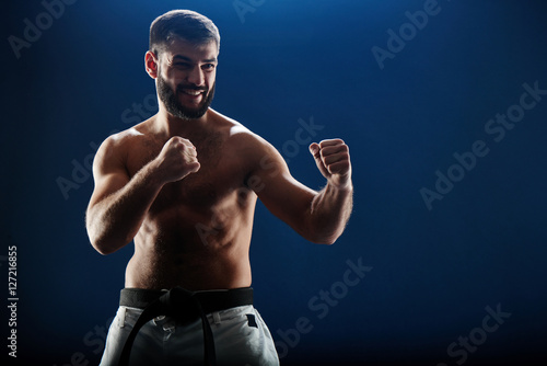 Schilderij op canvas Male karate bare torso in a fighting stance on a blue background